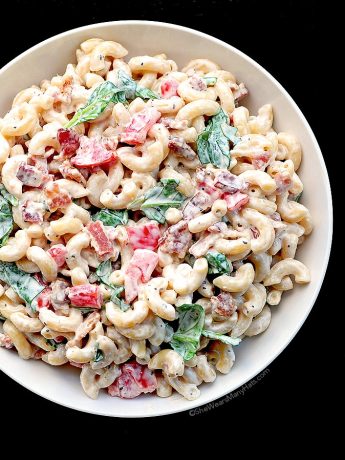 macaroni salad with spinach tomatoes and bacon on a white plate