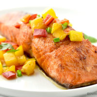 Sweet and Spicy Glazed Salmon on a white plate topped with pepper and peach relish